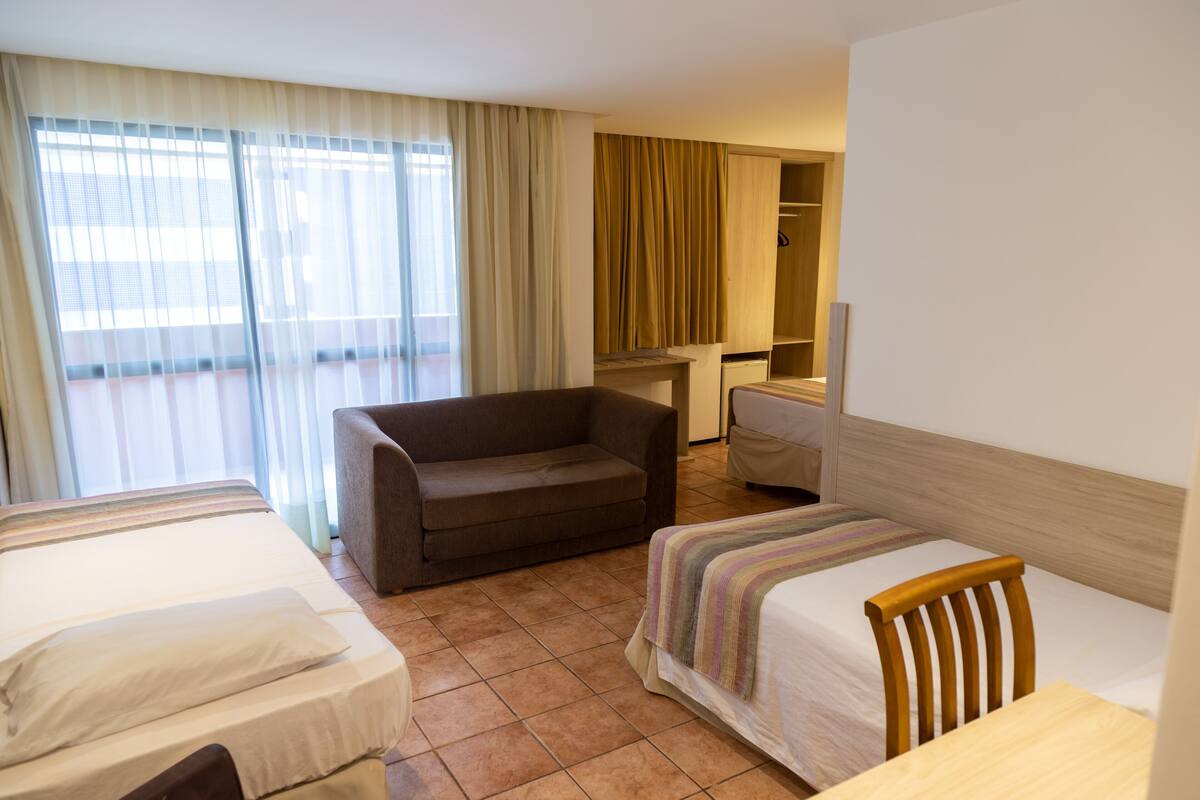 A hotel room with two beds, a sofa, a desk, and a wardrobe.