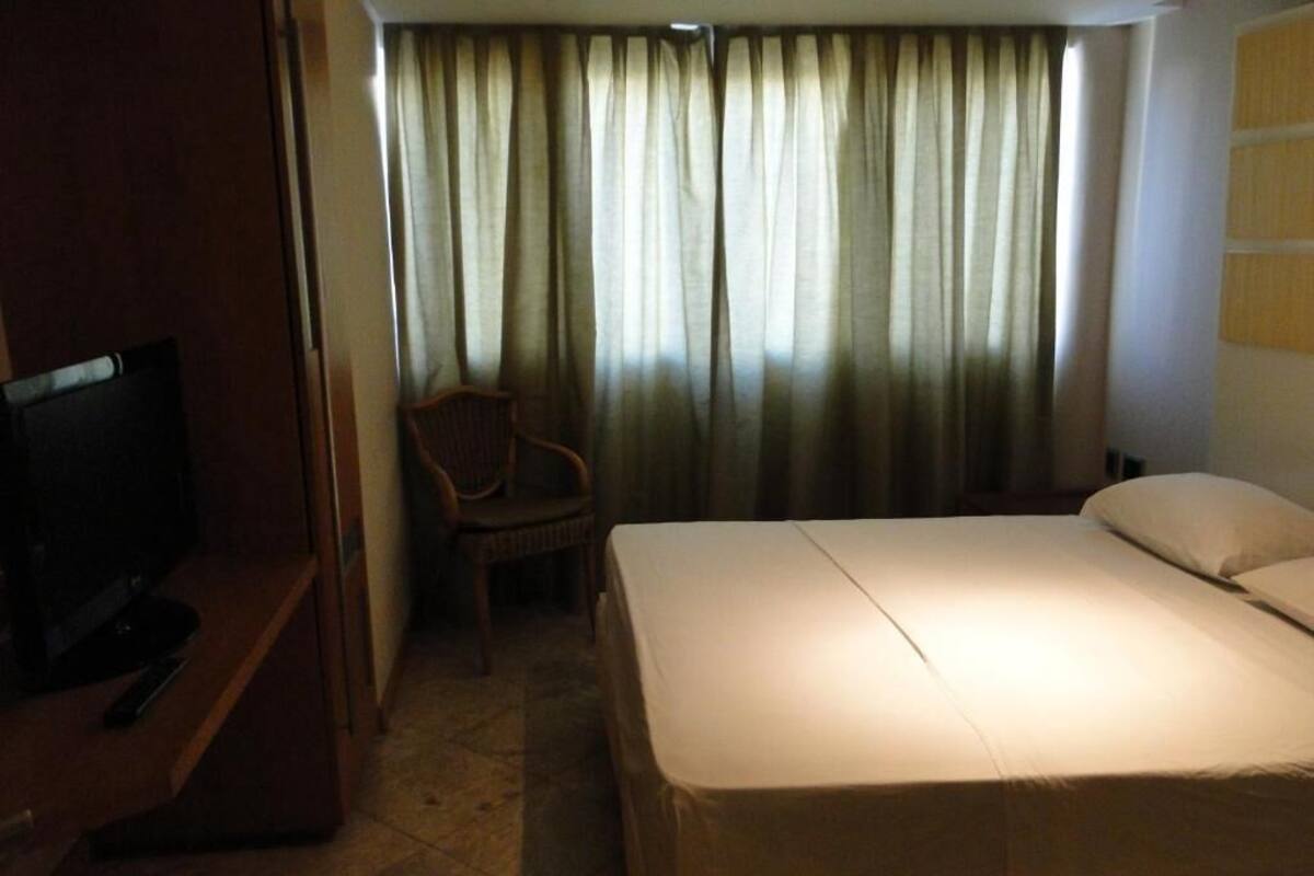 A hotel room with a bed, a chair, a television, and curtains.