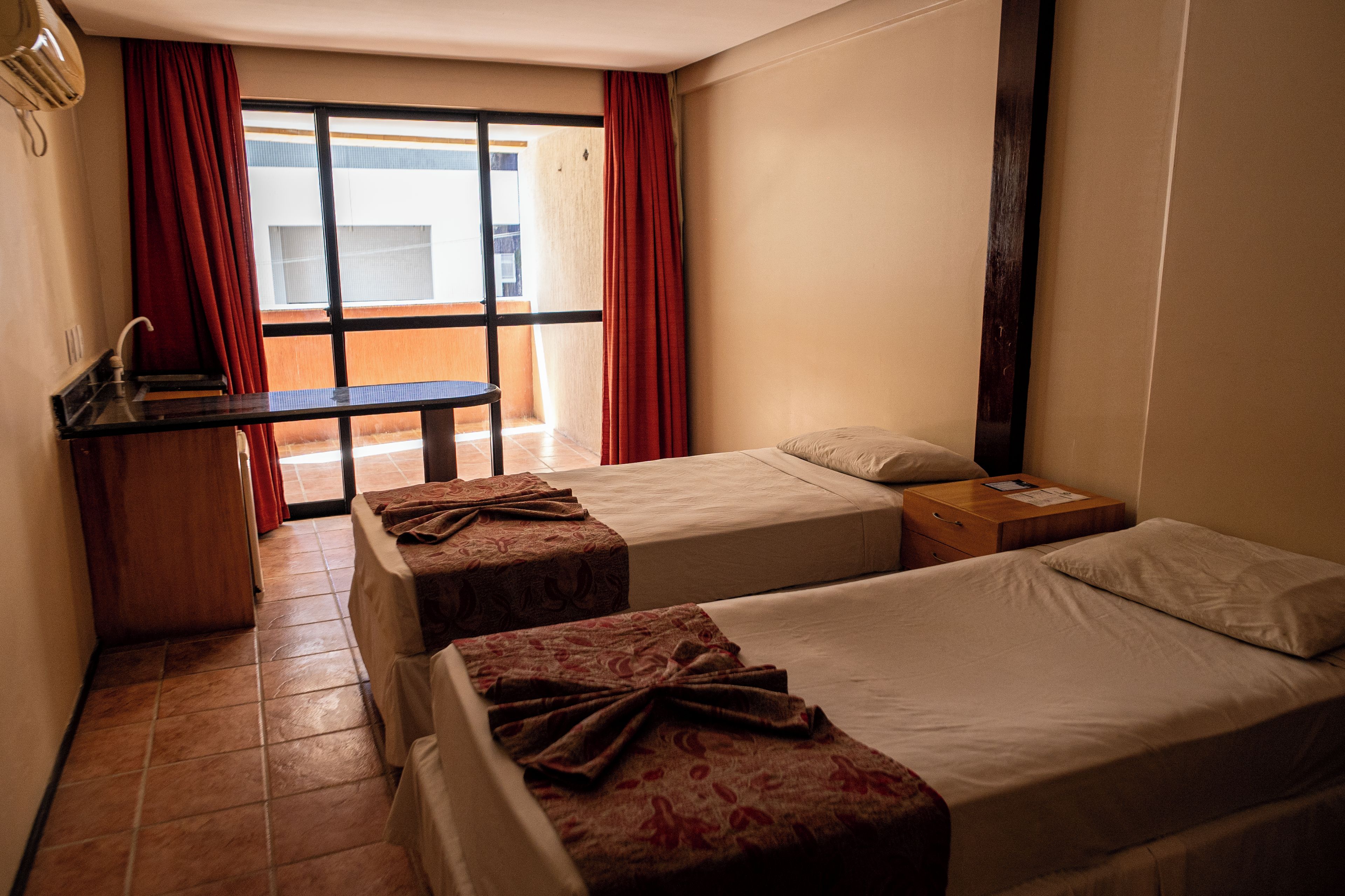 A hotel room with two beds, a small desk, and a window with curtains.