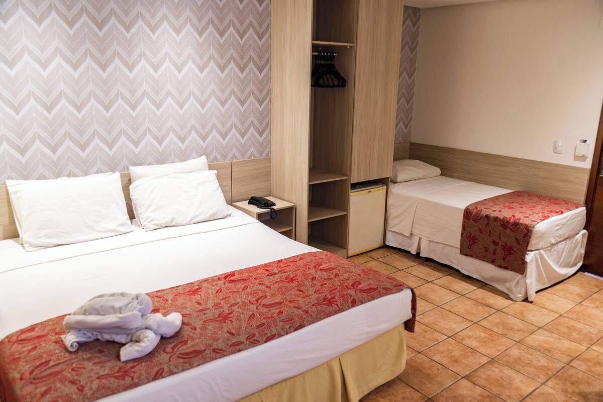 A hotel room with a large bed, a smaller bed, a wardrobe, and a nightstand.