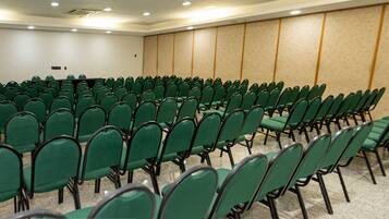 Sala de conferências com fileiras de cadeiras verdes e piso coberto por carpete.