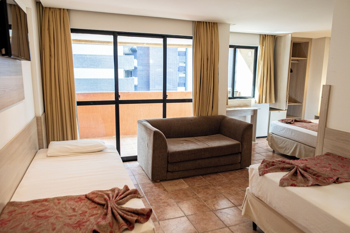 A hotel room with two beds, a sofa, a bathroom, and a view of buildings.