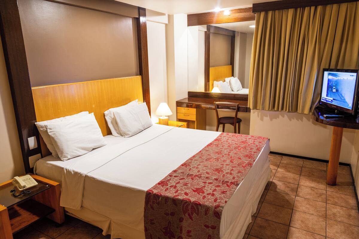 A hotel room with a bed, a desk, a chair, a television, and a telephone.