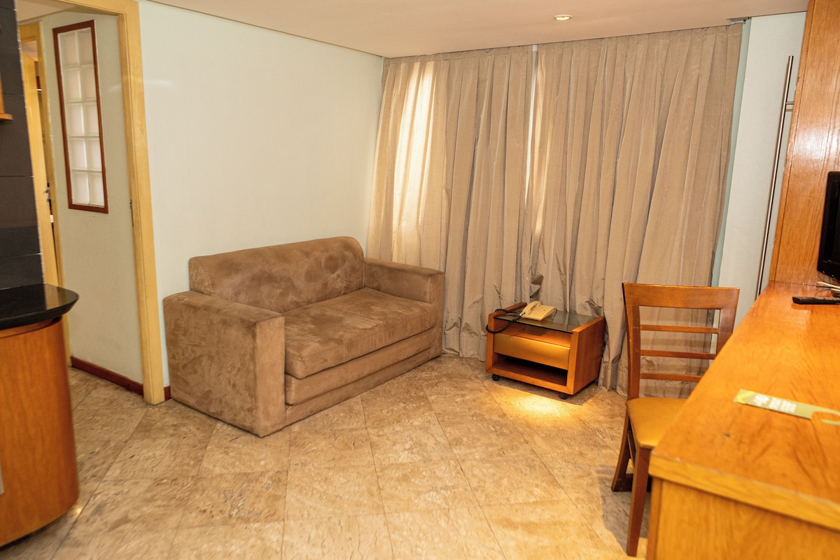 A living room with a sofa, a small table with a telephone, a wooden chair, and a television on a stand.