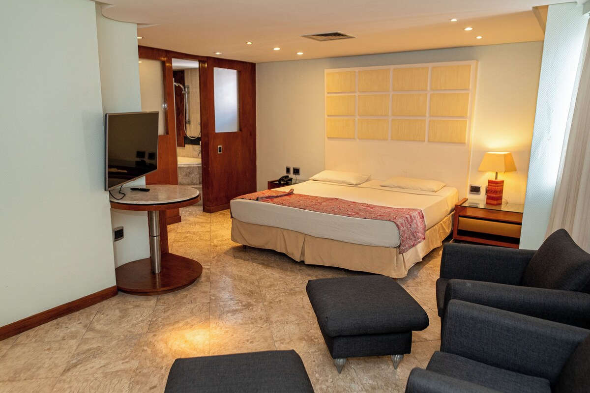 A hotel room with a bed, a TV, a desk, and a seating area.