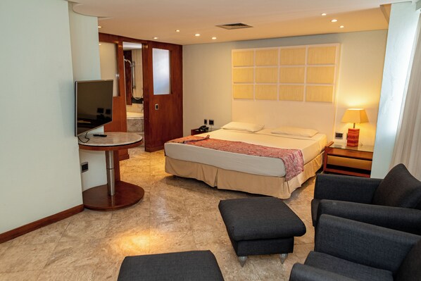 A hotel room with a bed, a TV, a desk, and a seating area.
