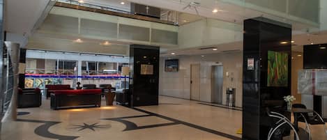 A spacious lobby with a reception desk, seating area, and a large glass window overlooking a street.