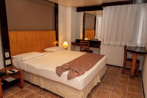 A hotel room with a bed, bedside table, lamp, and a desk with a chair. - Plaza Praia Suites (Fortaleza)