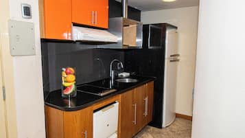 Cozinha compacta com bancada preta, armários de madeira, cuba de aço inoxidável e máquina de lavar louça branca.