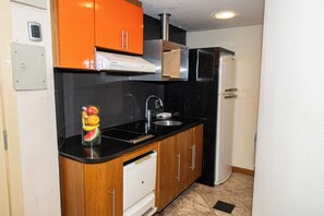 A compact kitchen with a black countertop, wooden cabinets, a stainless steel sink, and a white dishwasher.