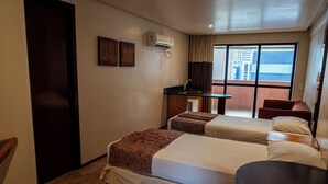 A hotel room with two beds, a small desk, a chair, and a window with a view of buildings. - Plaza Praia Suites (Fortaleza)