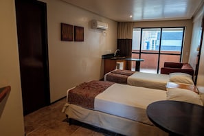 A hotel room with two beds, a small desk, a chair, and a window with a view of buildings. - Plaza Praia Suites (Fortaleza)