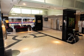 A hotel lobby with a reception desk, seating area, and a large decorative floor design. - Plaza Praia Suites (Fortaleza)