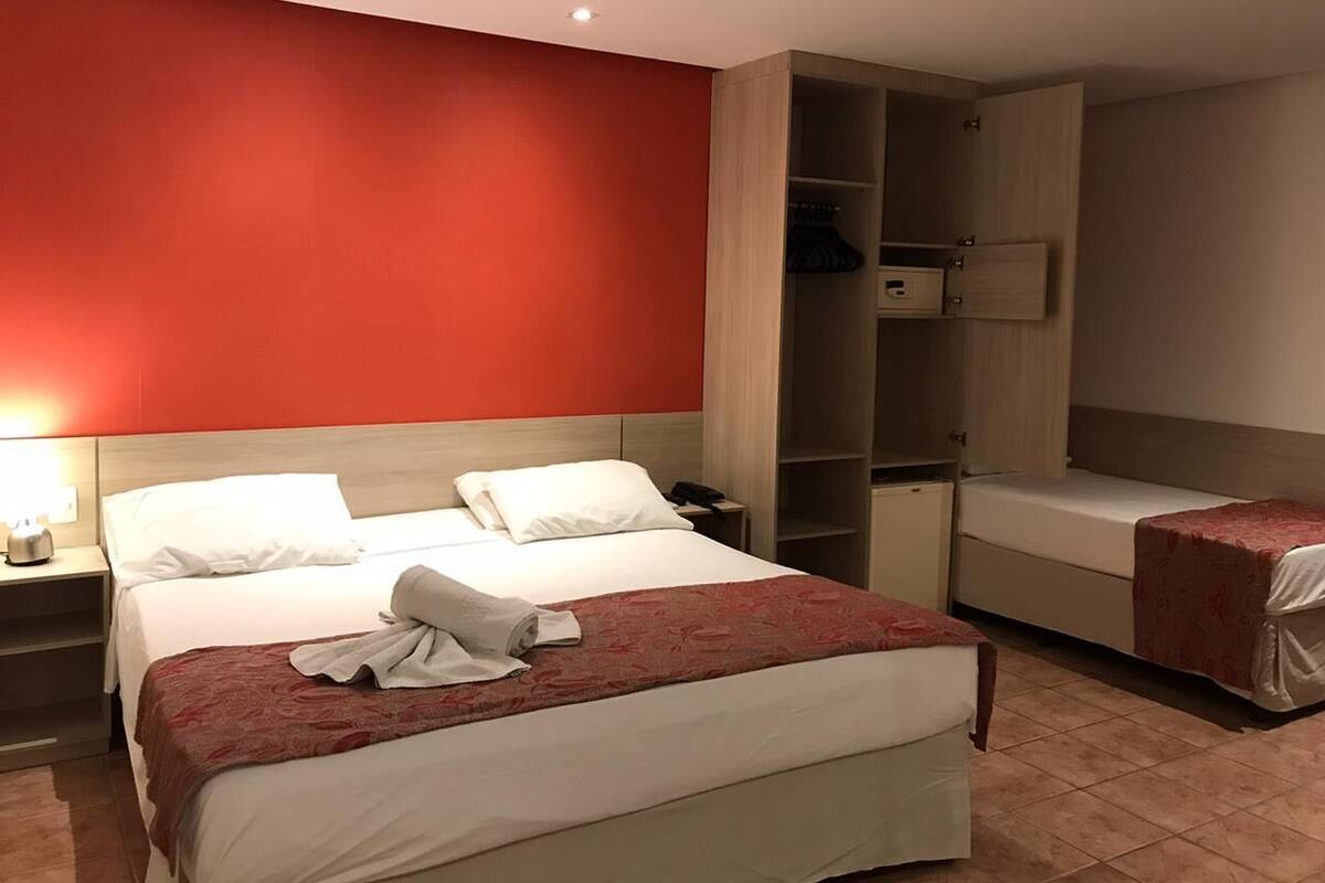 A hotel room with a large bed, a bedside table, a wardrobe, and a small desk.