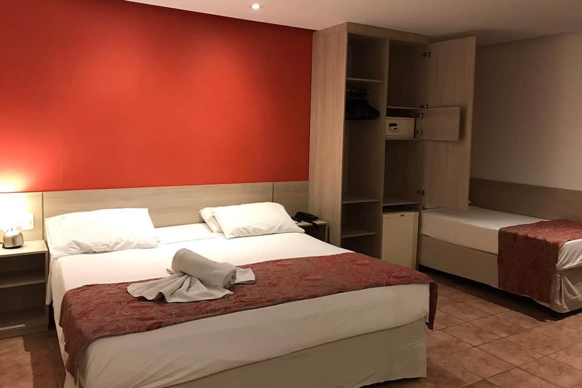 A hotel room with a large bed, a bedside table, a wardrobe, and a small desk.