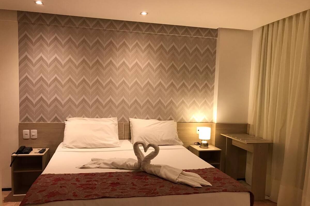 A hotel room with a bed, a nightstand, a lamp, and a wall with a chevron pattern.