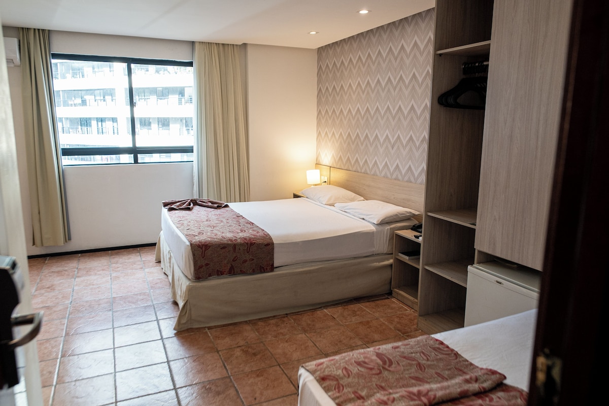 A hotel room with a bed, a nightstand, a wardrobe, and a window with curtains.
