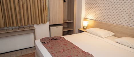 A hotel room with a bed, a nightstand with a lamp, a wardrobe, and a window with curtains.