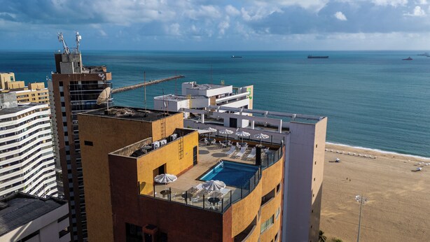 A rooftop pool area with lounge chairs and umbrellas, overlooking a beach and the sea. - Plaza Praia Suites (Fortaleza)