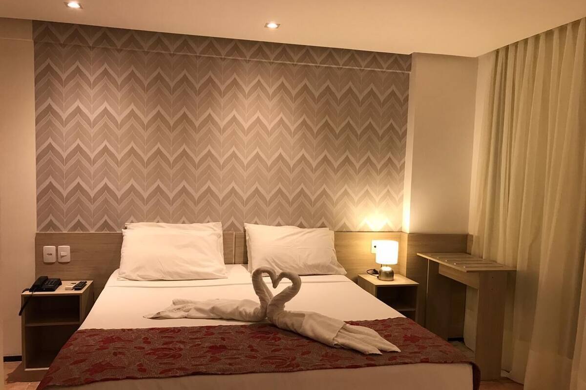 A hotel room with a bed, a nightstand, a lamp, and a wall with a chevron pattern.