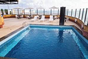 Una piscina con sillones de descanso y sombrillas, con vista a una masa de agua.