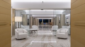 A modern hotel lobby with white leather chairs, a marble floor, and glass partitions.