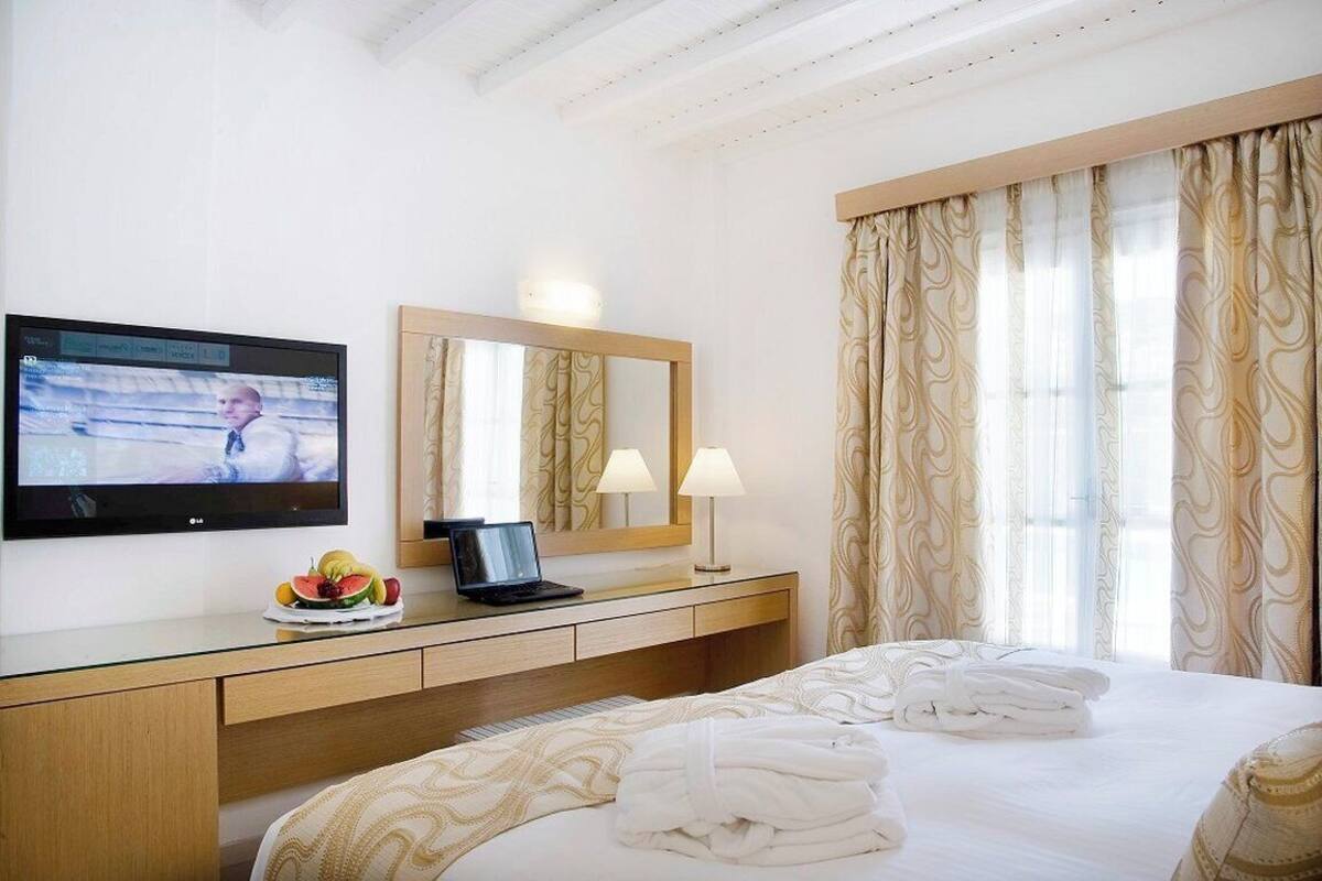 Una habitación de hotel con cama, escritorio, computadora portátil, televisor y espejo.