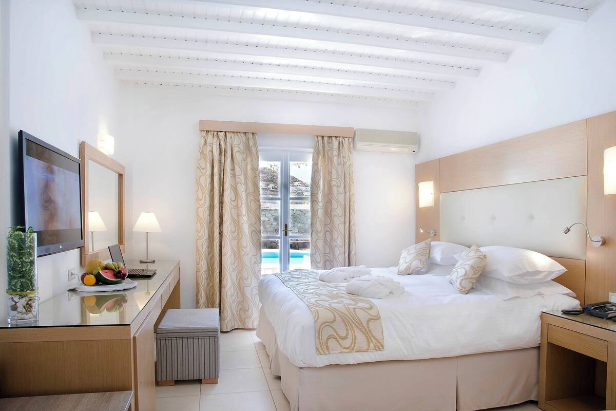 Habitación de hotel con cama, mesita de noche, escritorio con una computadora portátil y vistas al exterior.