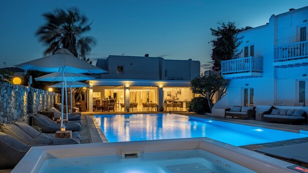 A swimming pool with lounge chairs and a hot tub, surrounded by a stone wall and a building with balconies.