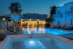 A swimming pool with lounge chairs and a hot tub, surrounded by a stone wall and a building with balconies. - Dionysos Luxury Hotel Mykonos (Mykonos)