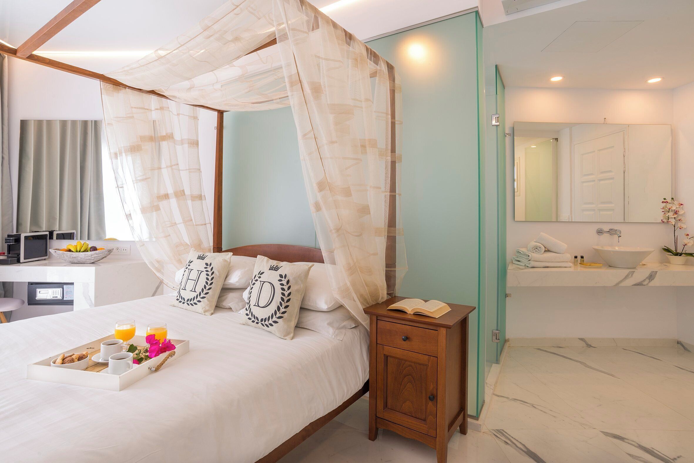 A hotel room with a bed, bedside table, and a bathroom with a sink and mirror.