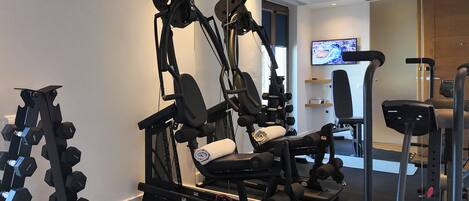 A home gym with a variety of exercise equipment including a bench press, dumbbells, and a cable machine.