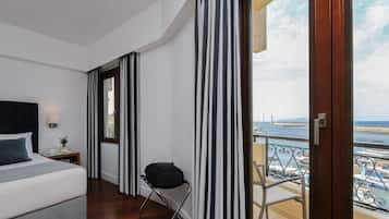 Une chambre d’hôtel avec un lit, une chaise, une fenêtre avec des rideaux et un balcon donnant sur la mer.