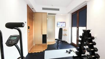 A gym with exercise equipment, a treadmill, a chair, and a television screen.