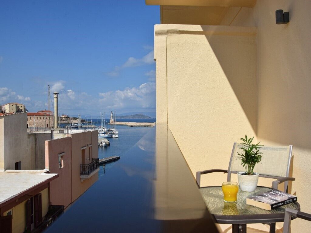 Un balcón con vistas a un puerto deportivo, una mesa con un vaso de jugo de naranja, un libro y una planta en maceta.