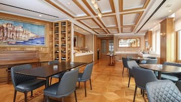 A spacious hotel lobby with a large wooden reception desk, multiple seating areas, and a large painting on the wall.