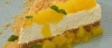 A slice of cheesecake with a crumbly topping and mango chunks, garnished with mint leaves.