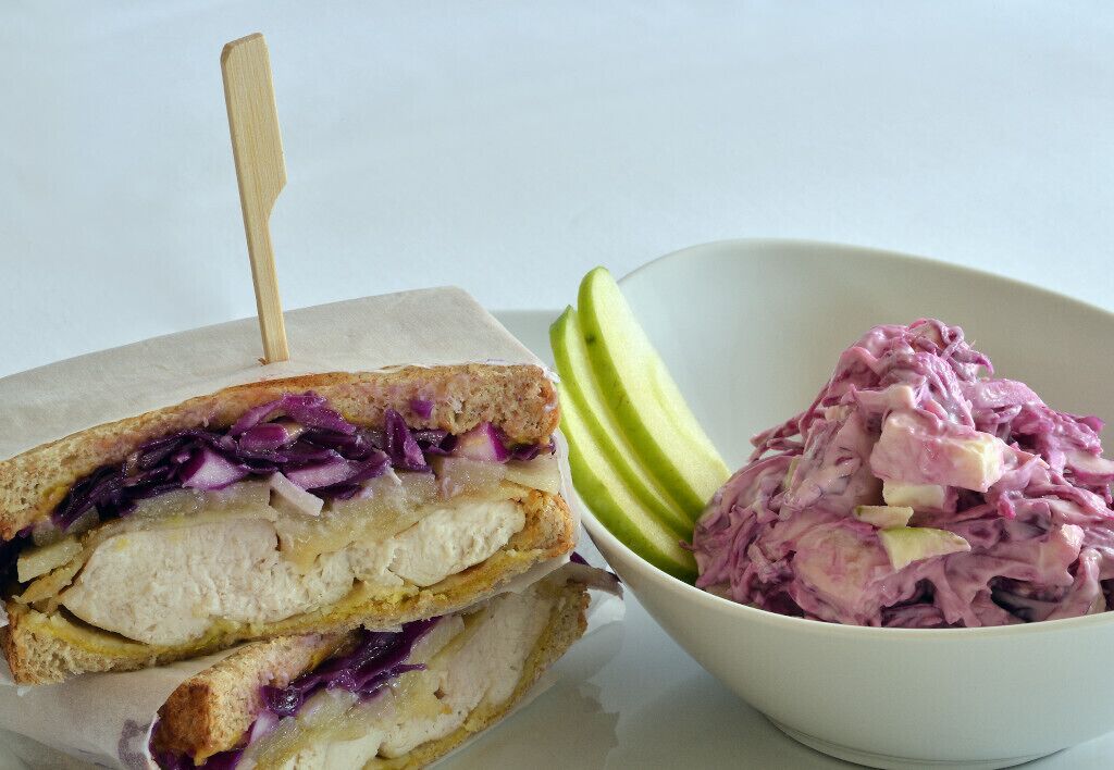 A sandwich with a toothpick, a bowl of coleslaw, and sliced apples.