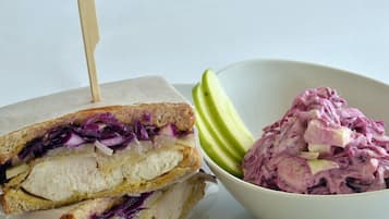 A sandwich with a toothpick, a bowl of coleslaw, and sliced apples.