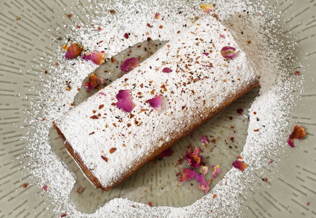 Postre con azúcar glasé y pétalos de rosa sobre un plato.