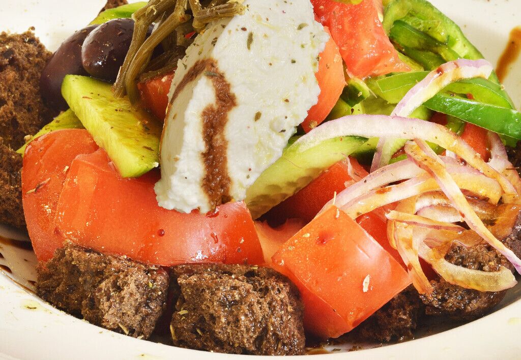 Ensalada con tomates, pepinos, cebollas, aceitunas y una cucharada de salsa blanca.