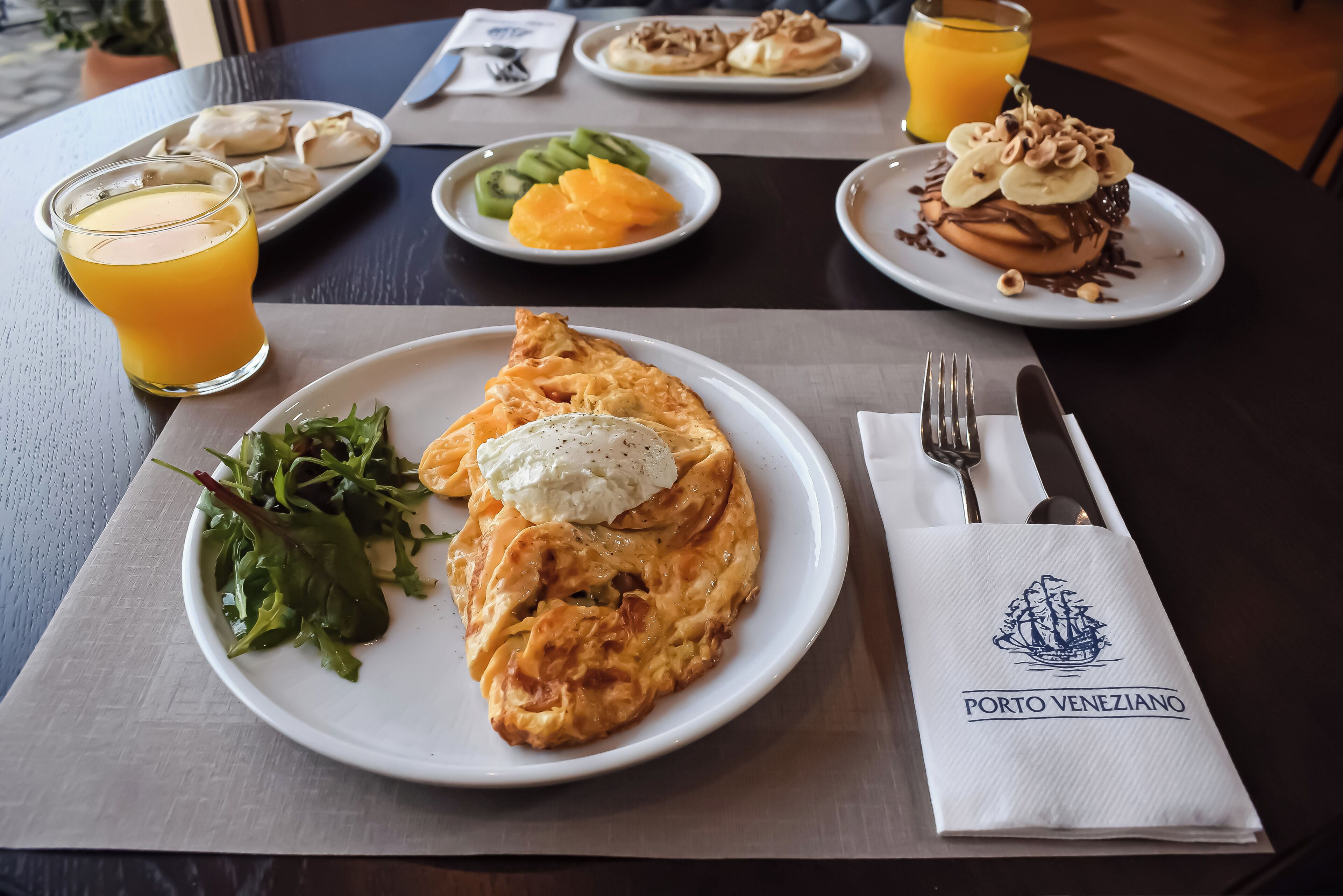 A table with plates of food, a glass of orange juice, and a napkin with a logo.