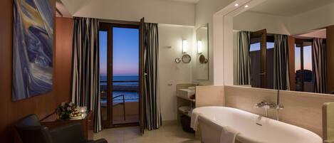 A modern bathroom with a bathtub, a large mirror, and a view of the ocean through the sliding glass door.
