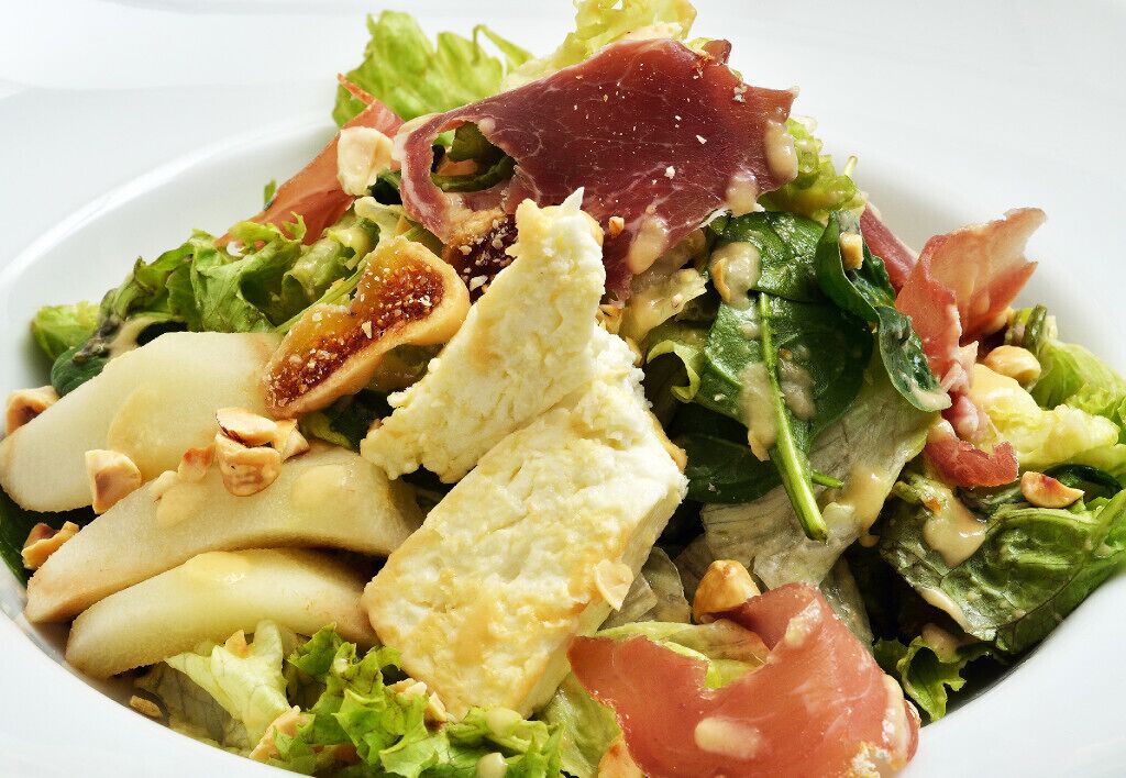 A salad with various ingredients including greens, nuts, and a piece of meat.