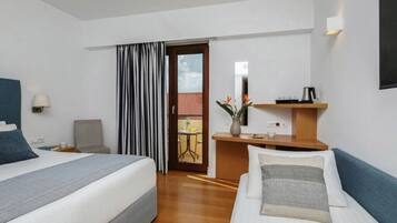 A hotel room with two beds, a desk, a chair, a small table, a mirror, and a view of the outside.