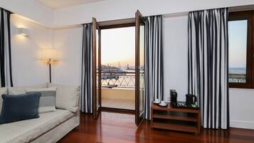 A hotel room with a sofa, a coffee maker, a lamp, and a view of the city through a glass door.