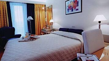 Ein Hotelzimmer mit einem großen Bett, einem Schreibtisch, zwei Stühlen, einer Lampe und einem Bild an der Wand.