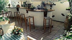 An outdoor bar area with a tiled floor, wooden stools, a checkered tablecloth, and potted plants. - The Park Hotel Piraeus (Piraeus)