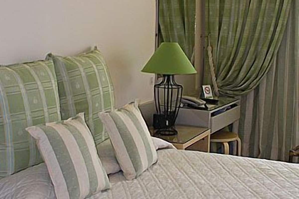 A neatly made bed with a quilted cover, a bedside table with a lamp, and a mirror above it.