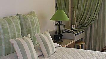 A neatly made bed with a quilted cover, a bedside table with a lamp, and a mirror above it.
